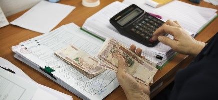 Eine Person hält Geld in der Hand und tippt auf einem Taschenrechner.