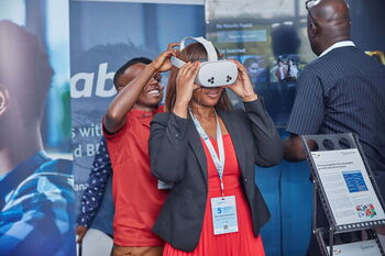 Eine Frau bekommt an einem Messestand eine VR-Brille angezogen.