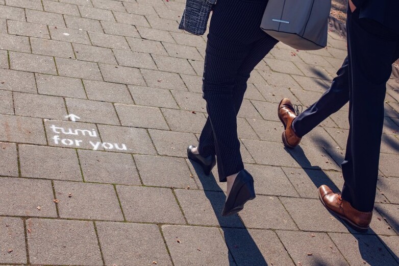 Zwei Personen laufen auf einem Bürgersteig, auf den „tumi for you“ gesprüht wurde.