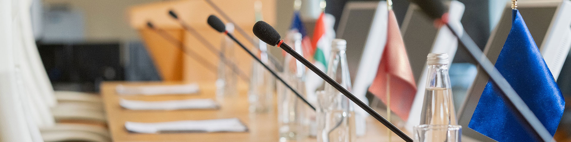 Mikrofone stehen auf einem Tisch neben verschiedenen Nationalflaggen.