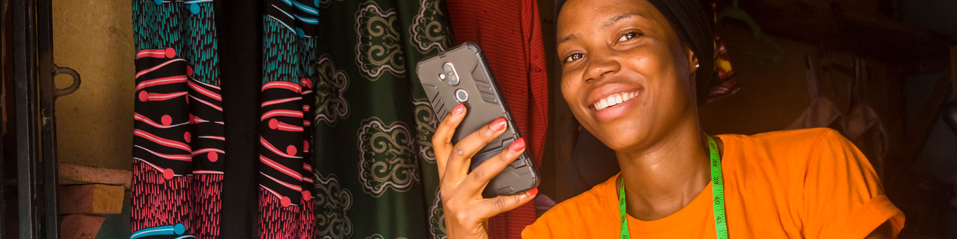 A young African woman smilingly holds a mobile phone in her hand