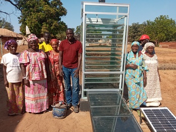 Un groupe d’hommes et de femmes sont rassemblés autour d’un séchoir solaire dans un village.