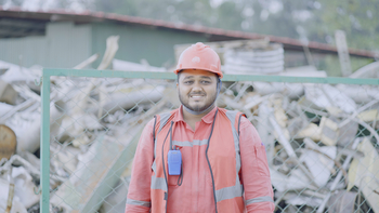 A factory worker in PPE stands in front of a fence. (Photo: GIZ/Noor Alam)